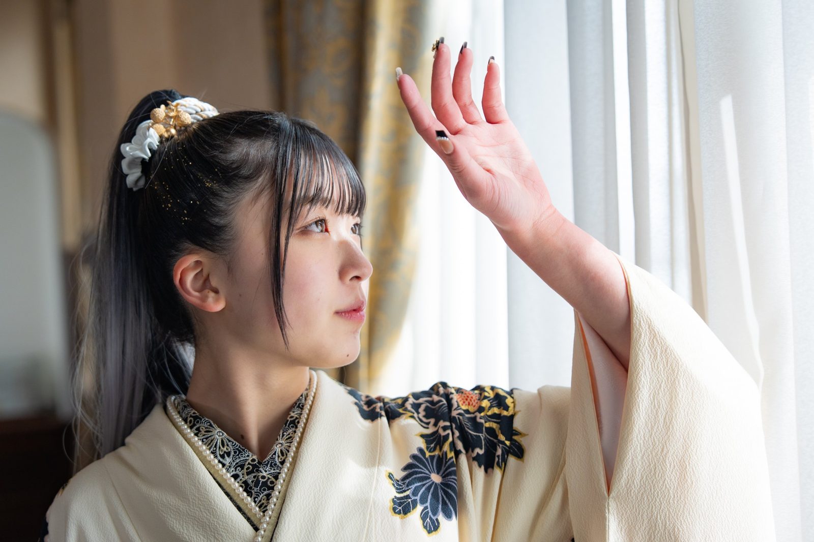 窓辺の光に手をかざす振袖姿の女性
