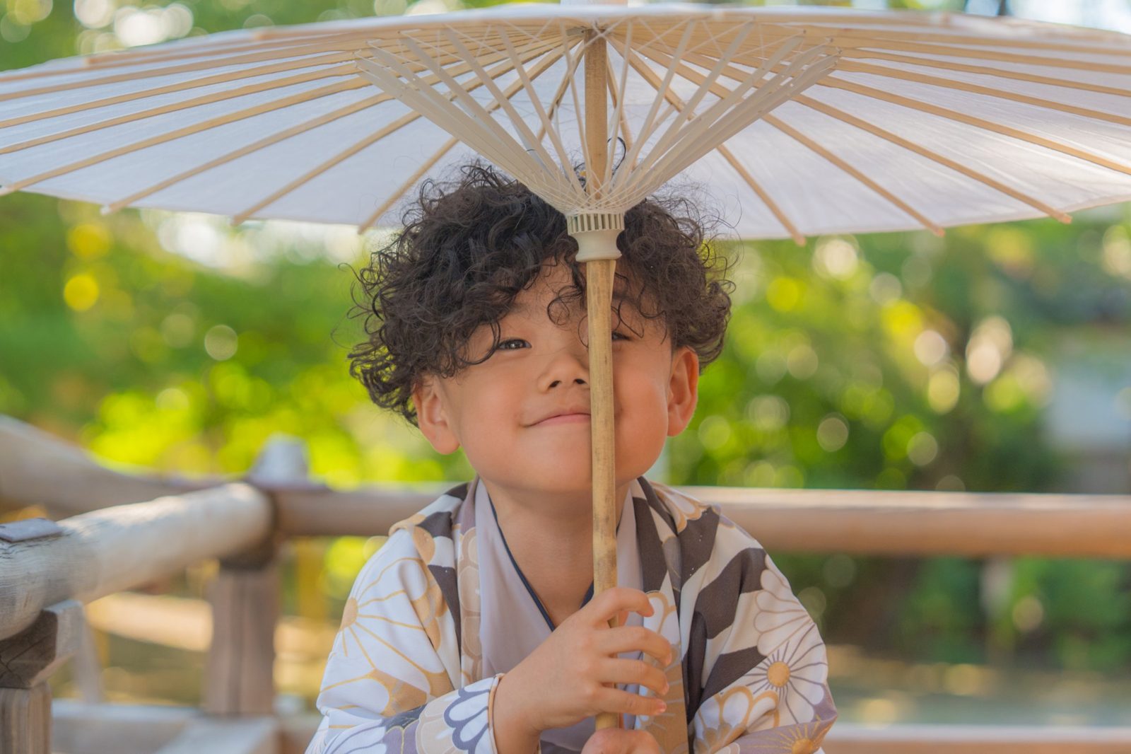 和傘の柄で顔を半分隠してほほえむ男の子