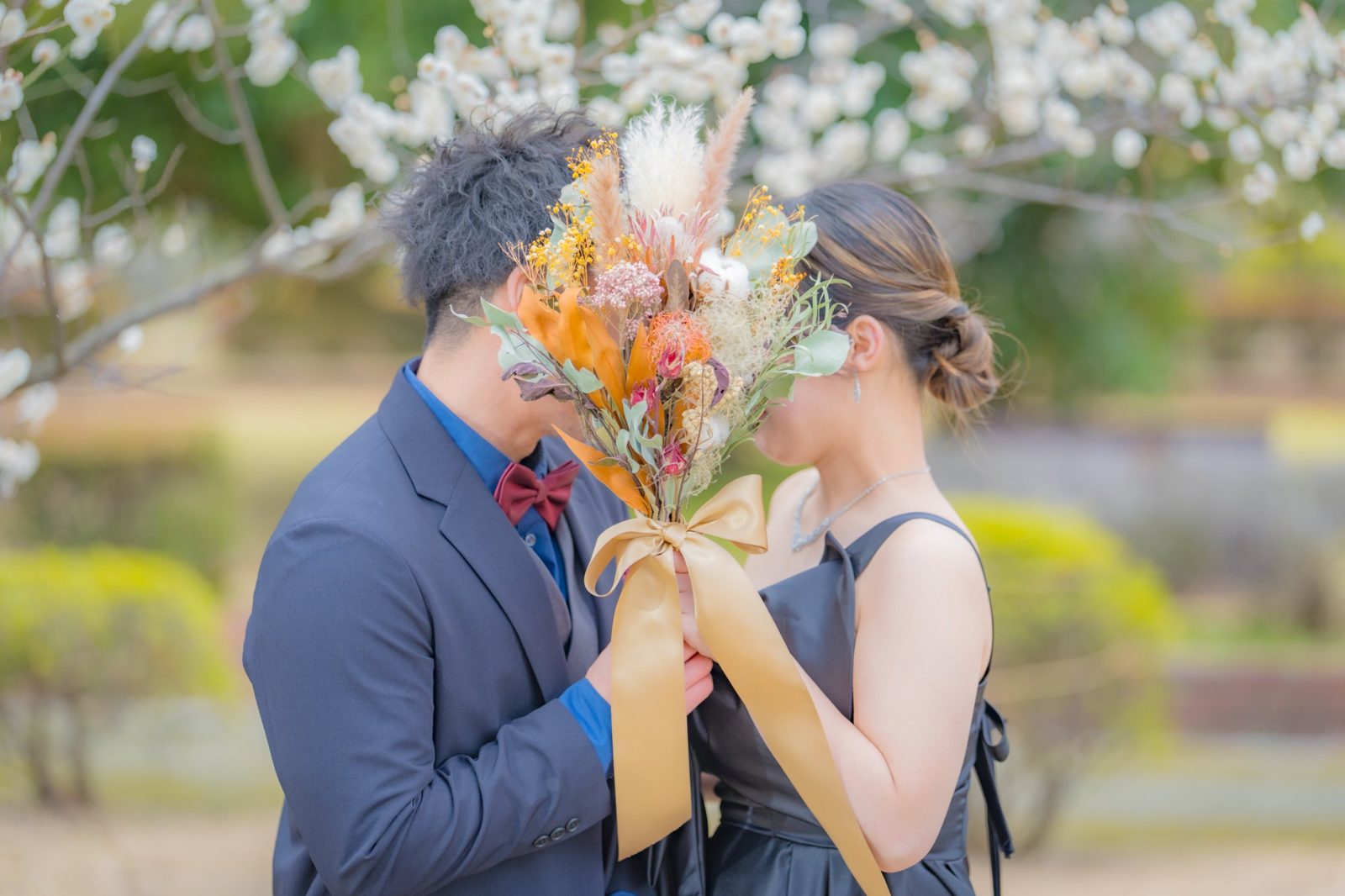 梅の花の下、ブーケで顔を隠すふたり