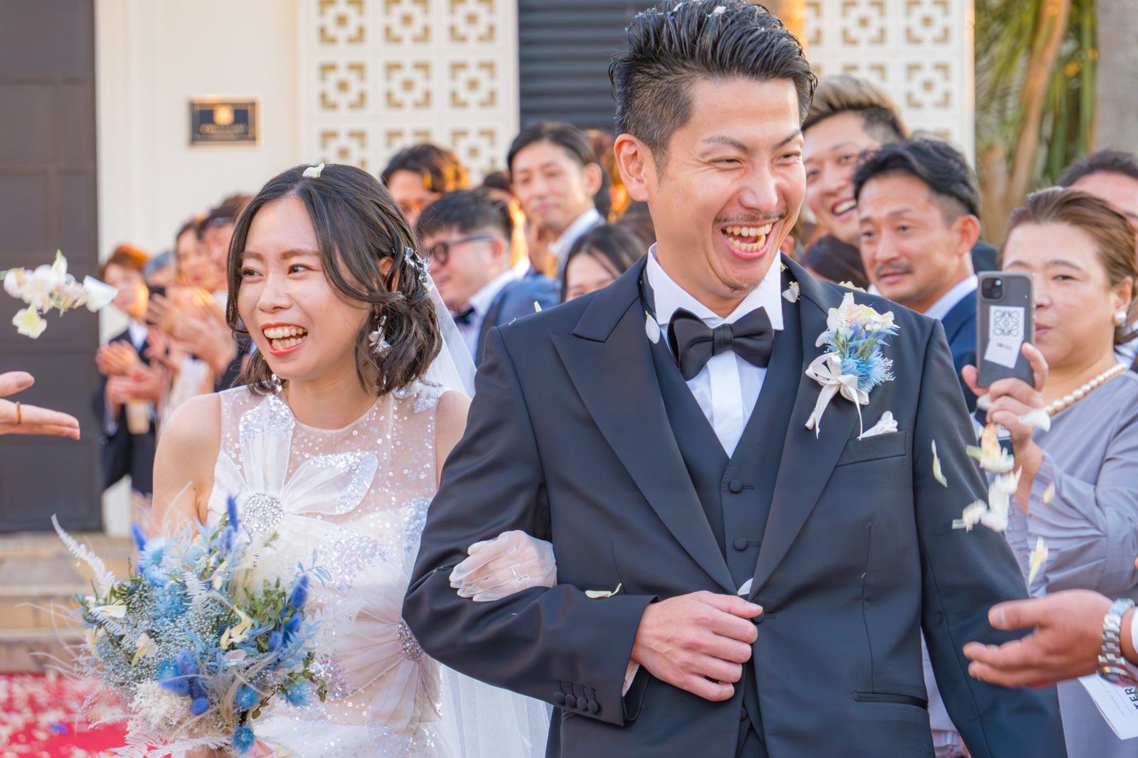フラワーシャワーの中を大笑いで歩く新郎新婦